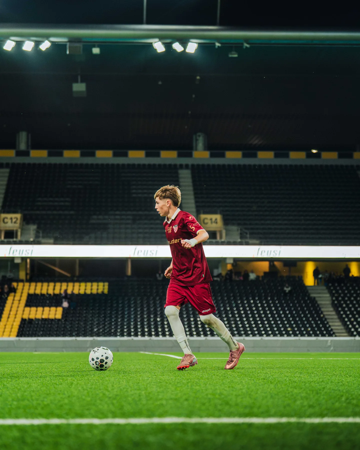 Spieler in Rot läuft vor der leeren Tribüne mit dem Ball
