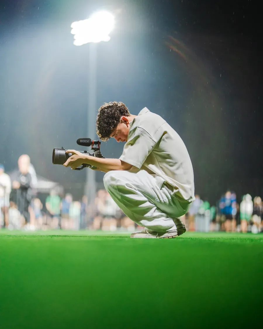 Levin hockt am Spielfeldrand und fotografiert, dahinter der Flutlichtmast