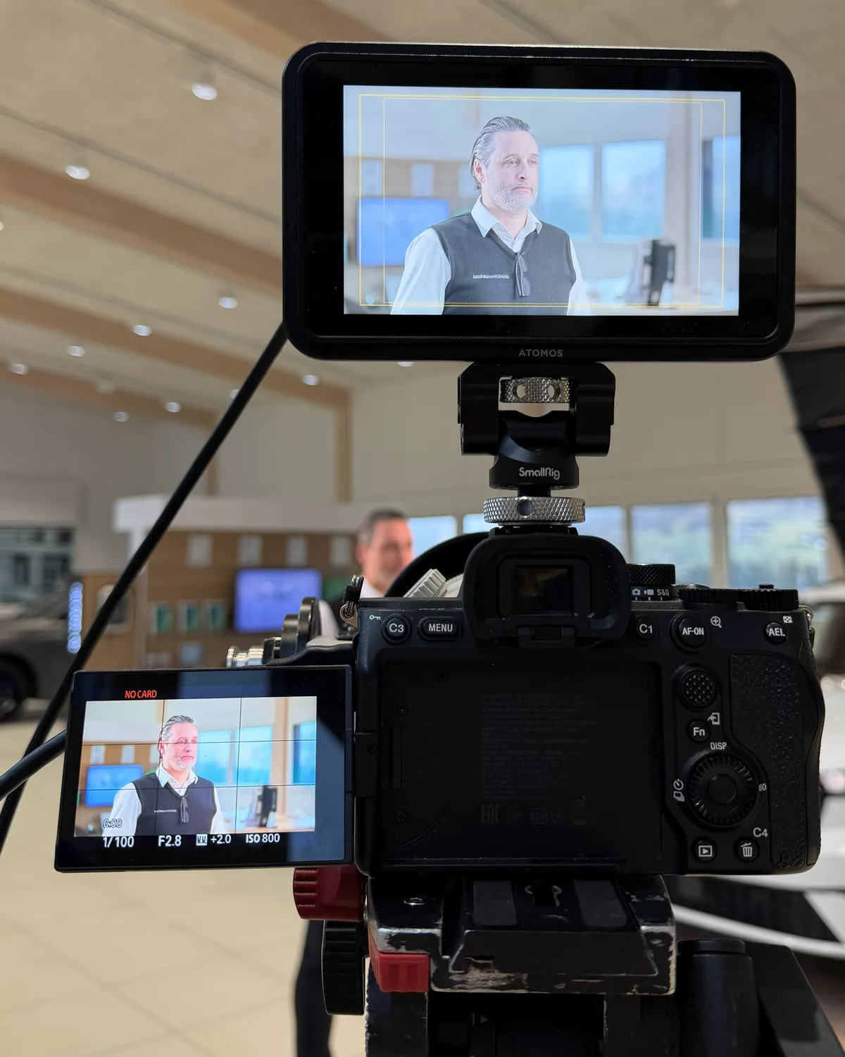Blick über Monitor und Kamera auf den Verkaufsleiter im Showroom